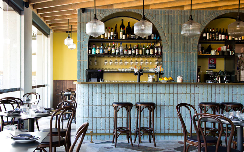 Sella VInoteca bar interior, mustard wall, blue bricks, brown chairs, hanging pendants